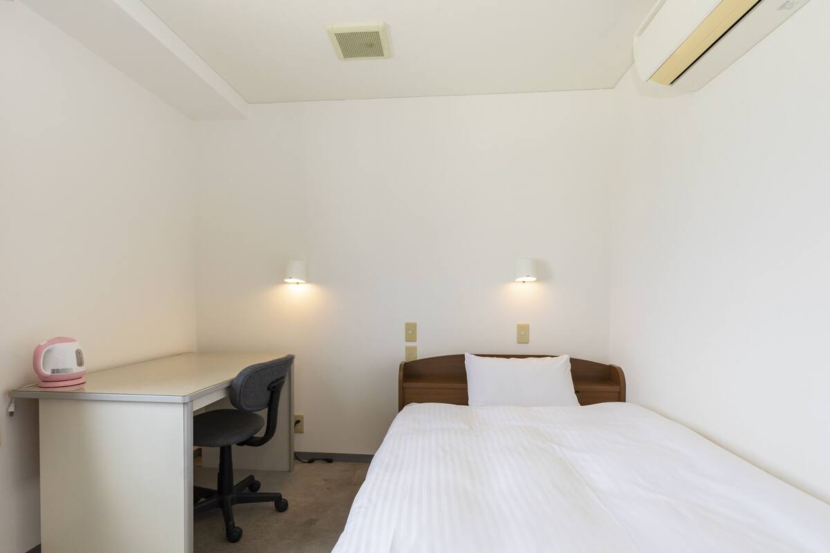 A hotel room with a bed, a desk, and two wall-mounted lights.
