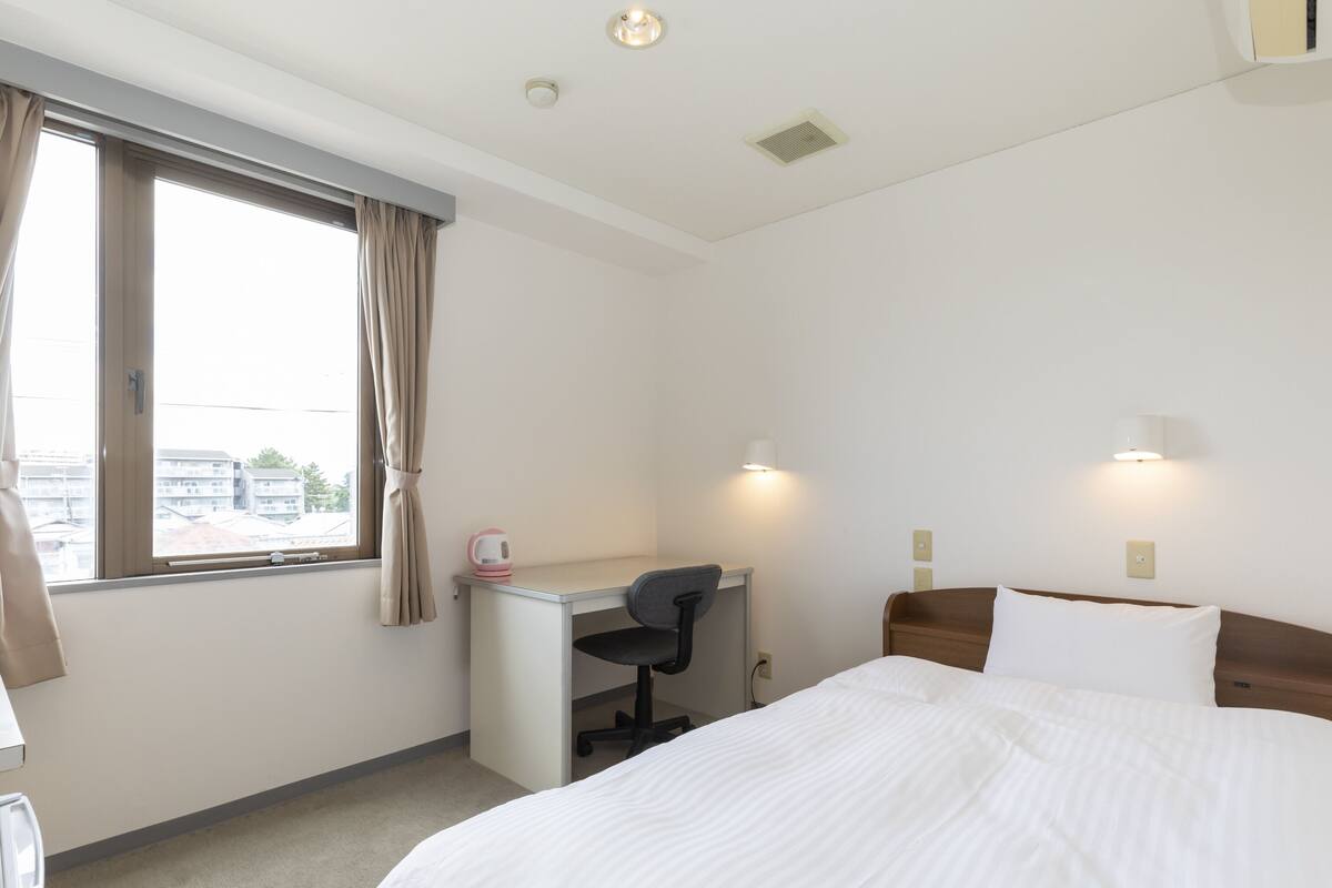 A hotel room with a bed, desk, chair, and two wall-mounted lamps.