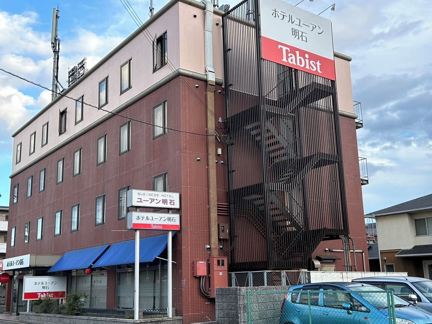 Un hotel de negocios con un llamativo letrero de Tabist en la fachada, varias ventanas y un toldo azul sobre la entrada.