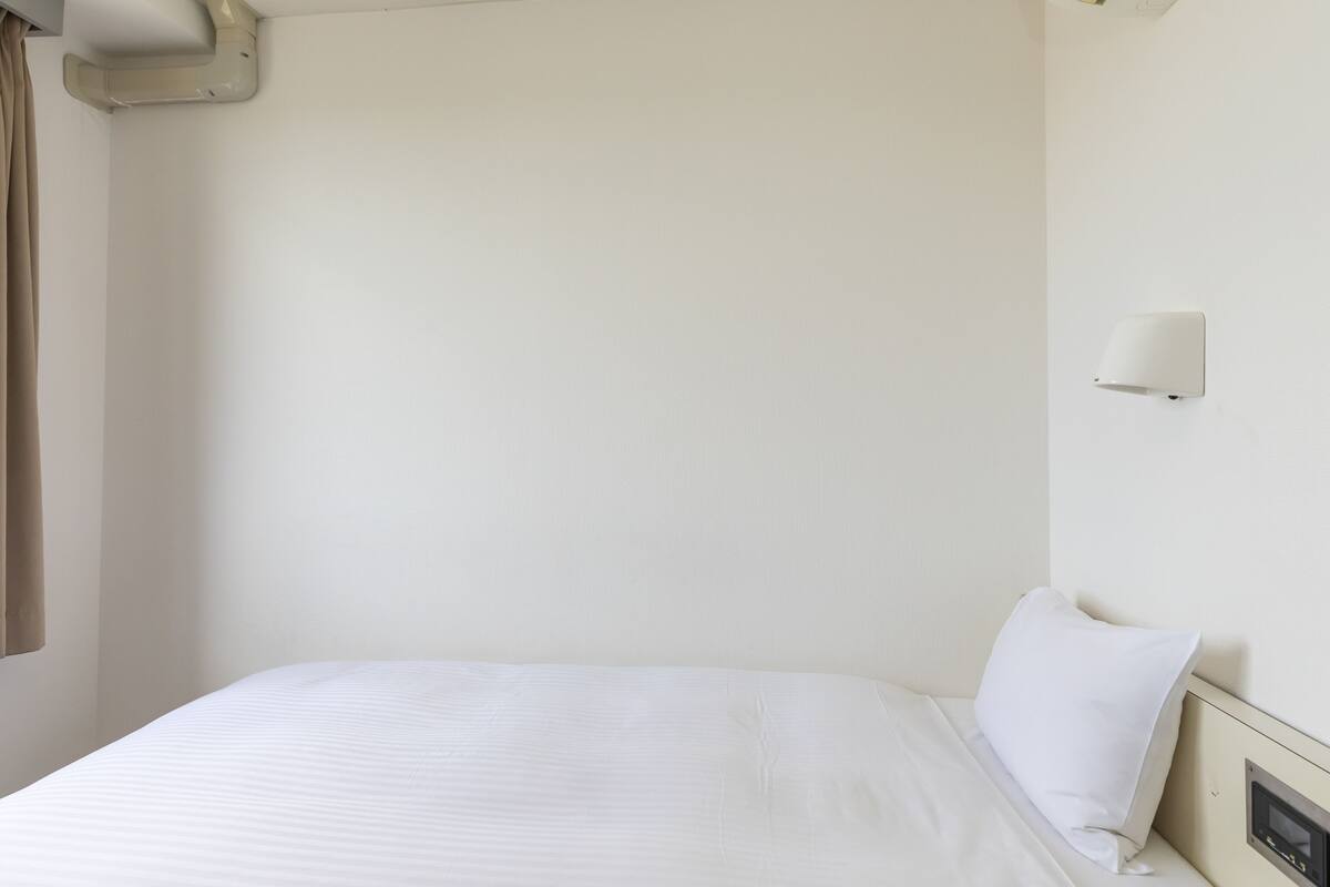 A hotel room with a bed, a wall-mounted light, and a control panel.