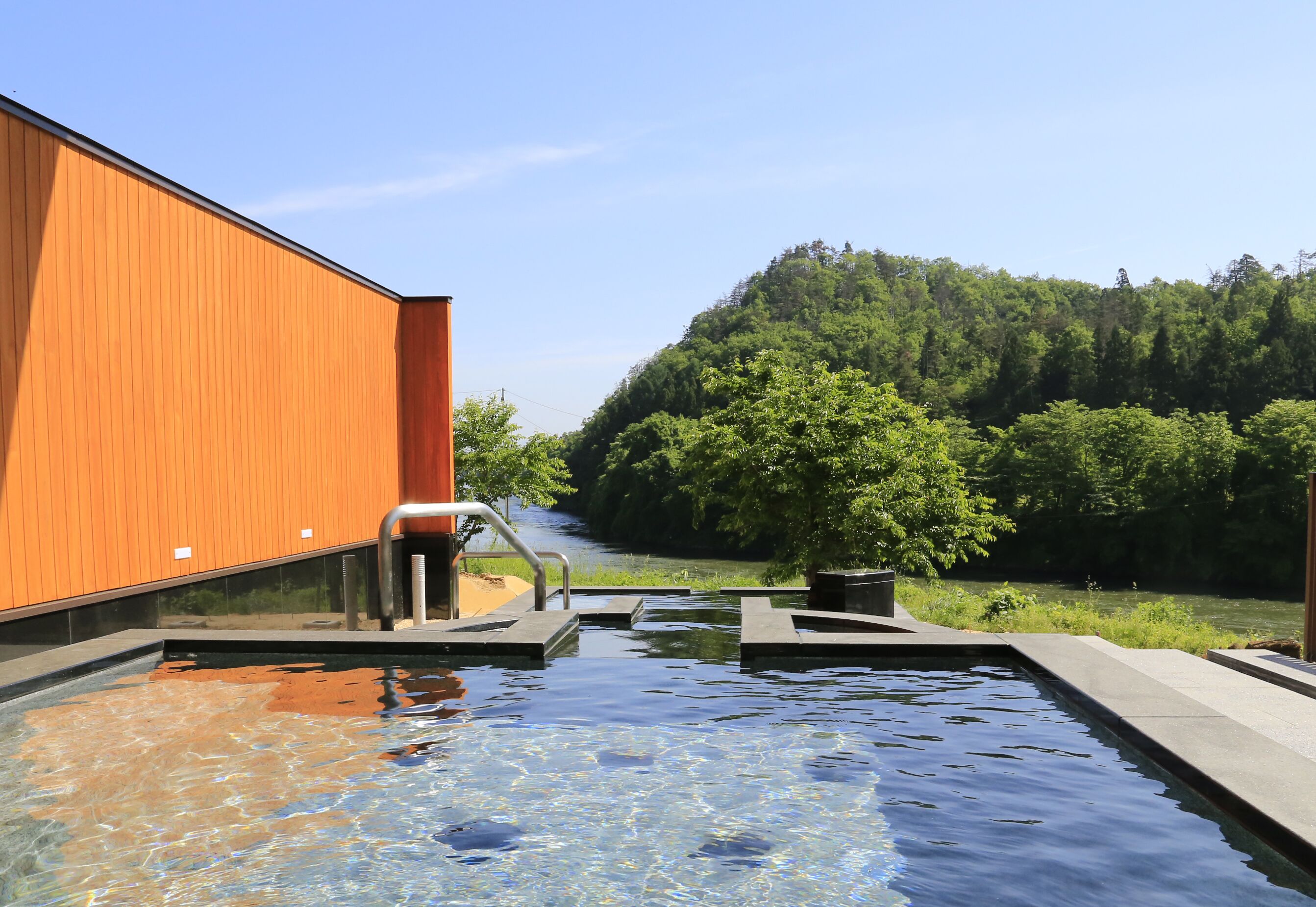 Una piscina con un edificio de madera y una colina boscosa al fondo.