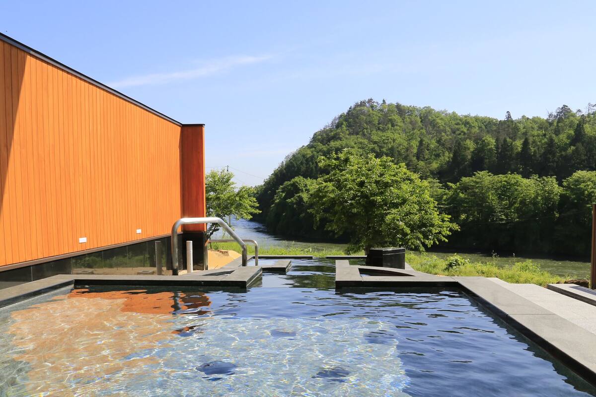 A swimming pool with a wooden building and a forested hill in the background.