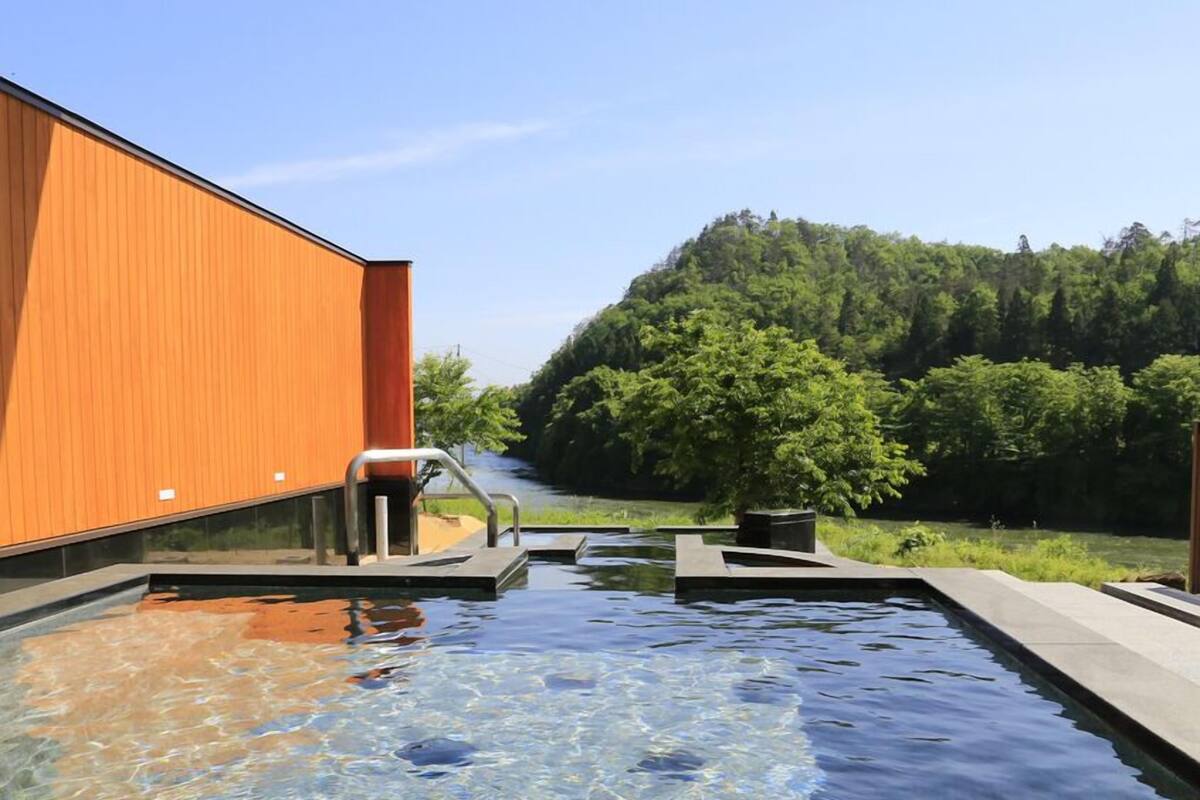 A swimming pool with a wooden building and a forested hill in the background.