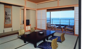 Een kamer met een donker houten tafel, gestreept beklede stoelen, een televisie en uitzicht op de oceaan.