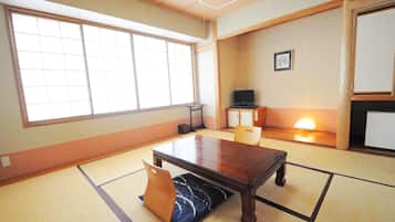 A traditional Japanese room with tatami flooring, a low table, a chair, a small desk with a laptop, and a wall-mounted shelf.