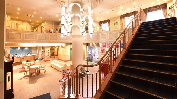 A spacious hotel lobby with a central staircase, multiple seating areas, and a well-lit ceiling design. - Shibetsu Inn Suigetsu (Shibetsu)