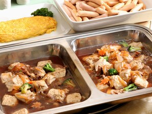 A buffet with various dishes including a large omelette, sausages, and a meat dish with vegetables.