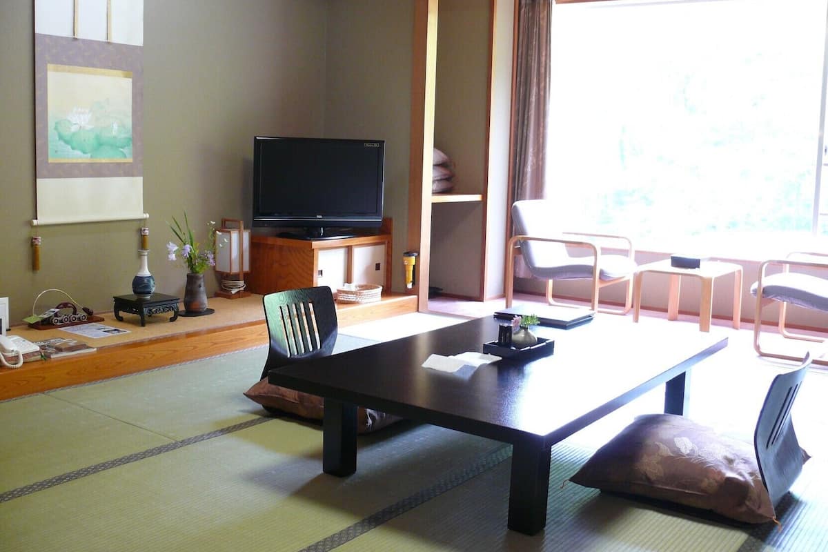 Un salón japonés tradicional con suelo de tatami, una mesa baja, un televisor y una puerta corredera que da a un balcón.