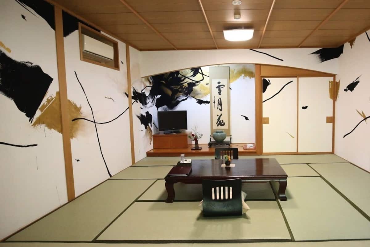 Una habitación japonesa tradicional con suelo de tatami, una mesa de madera baja, un televisor y una puerta corredera.