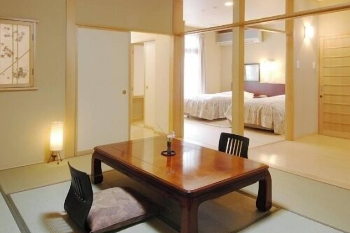 Una habitación tradicional japonesa con suelo de tatami, una mesa de madera y una cama con colcha blanca.