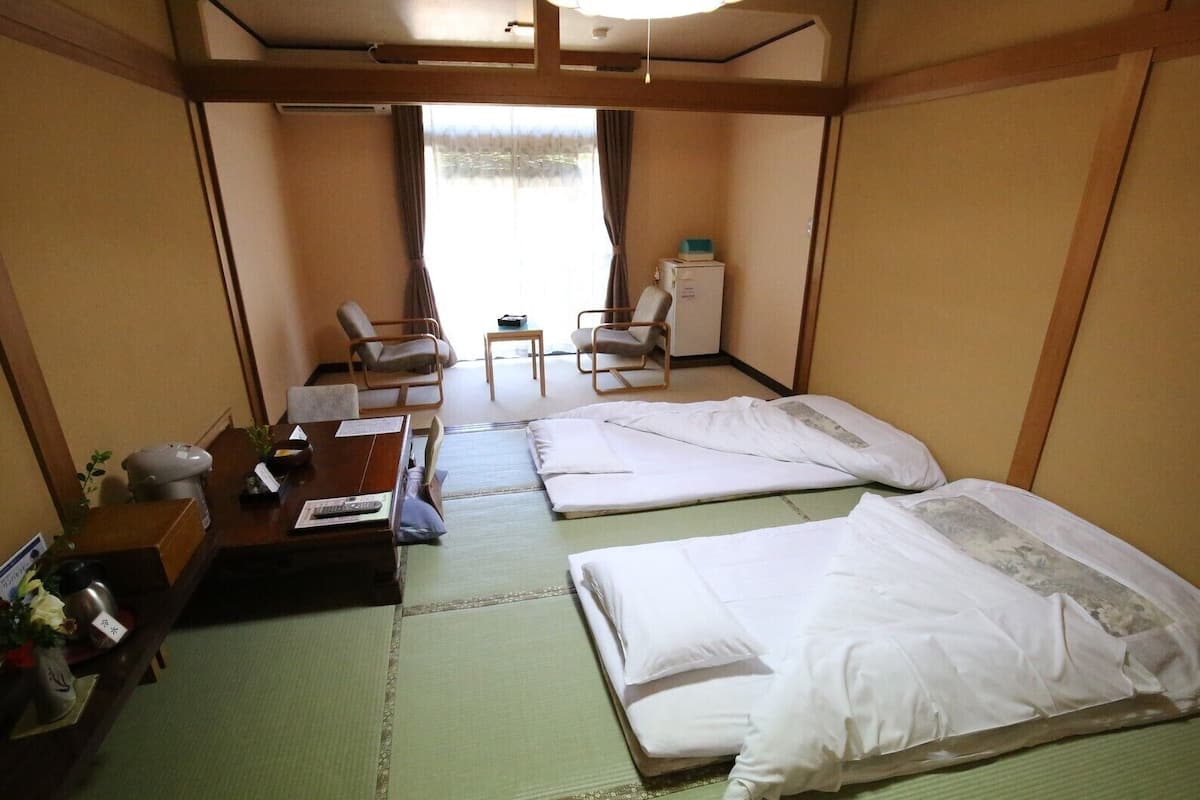Una habitación de hotel con dos camas, un escritorio con silla, una mesita y una ventana con cortinas.