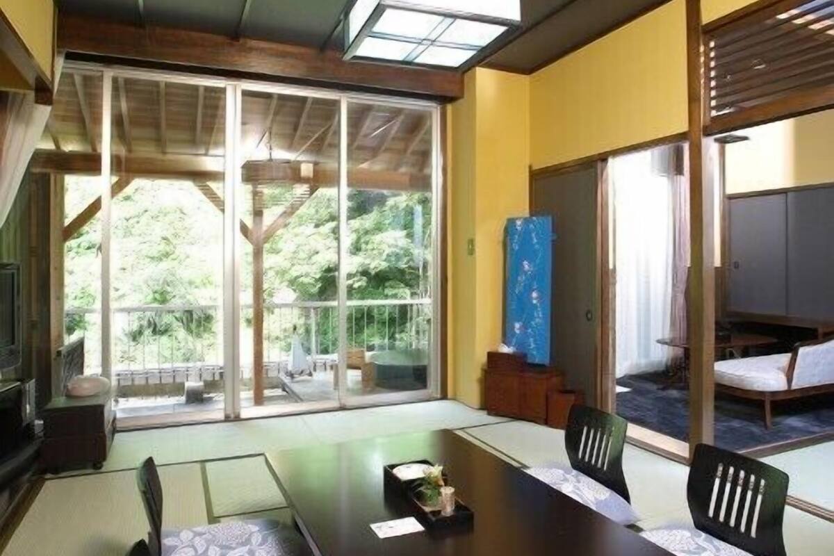 Una habitación de estilo japonés tradicional con suelo de tatami, una mesa baja y puertas correderas que dan a un espacio exterior.