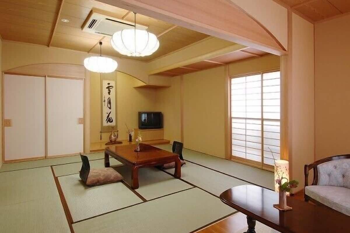 Una habitación tradicional japonesa con suelo de tatami, una mesa baja, un sofá y un televisor.