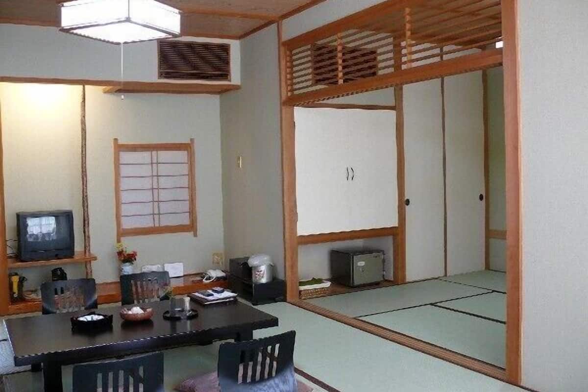 Una habitación tradicional japonesa con suelo de tatami, una mesa baja con sillas, un televisor y una puerta corredera.