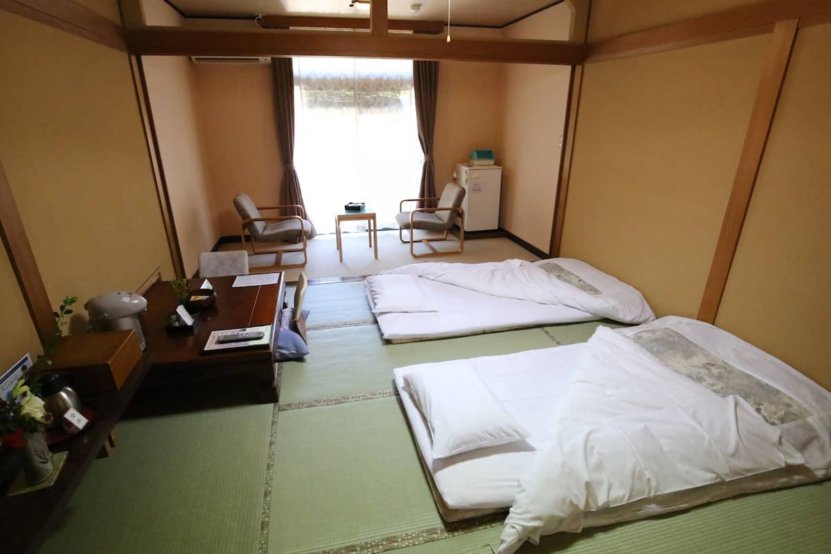 Habitación de hotel con dos camas, un escritorio, una silla, una mesita y un ventanal con cortinas.