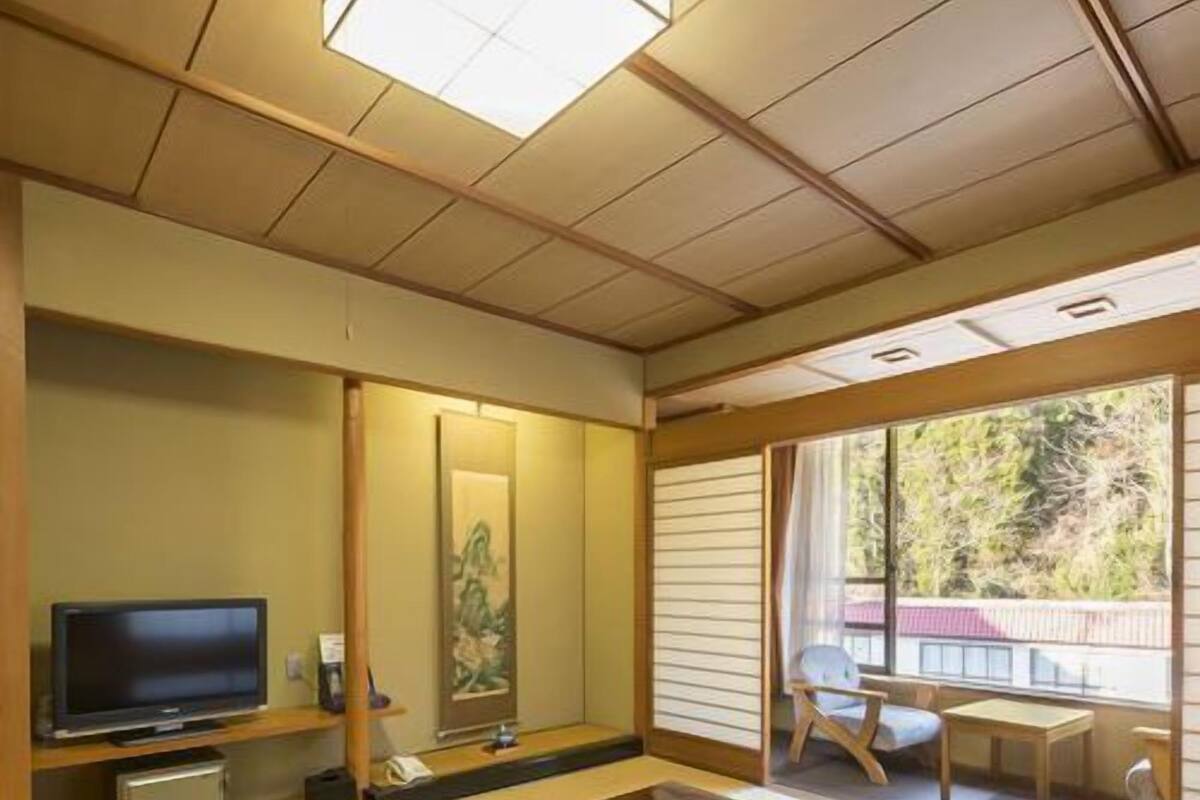 Una habitación japonesa tradicional con suelo de tatami, una mesa baja, un televisor y una puerta corrediza que da a un espacio exterior.