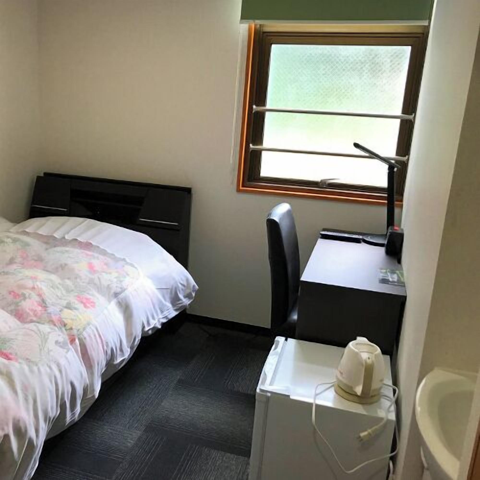 Een kleine hotelkamer met een bed, een bureau, een stoel, een klein tafeltje en een raam.