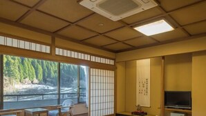A tatami mat room with a tatami mat table, a television, and a view of a river.