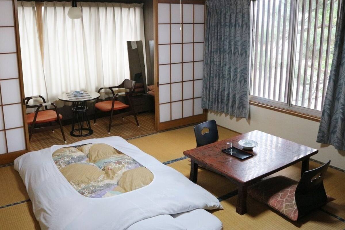 A traditional Japanese room with tatami flooring, a low table, a bed with a futon, and sliding doors.