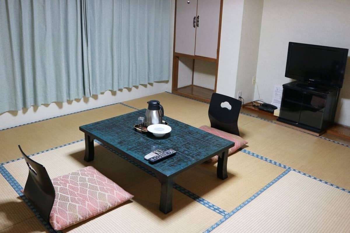 A room with tatami flooring, a table with a remote control, a kettle, and a television on a stand.