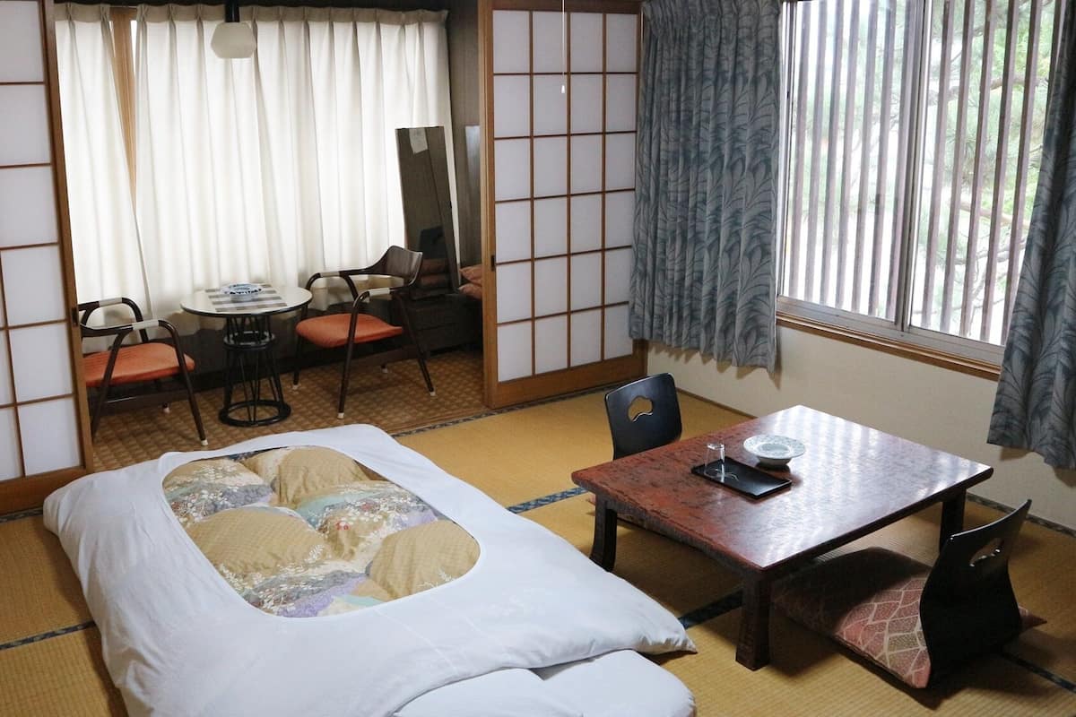 A traditional Japanese room with tatami flooring, a futon bed, a small table with a tray, and a view of the outdoors through a shoji screen.