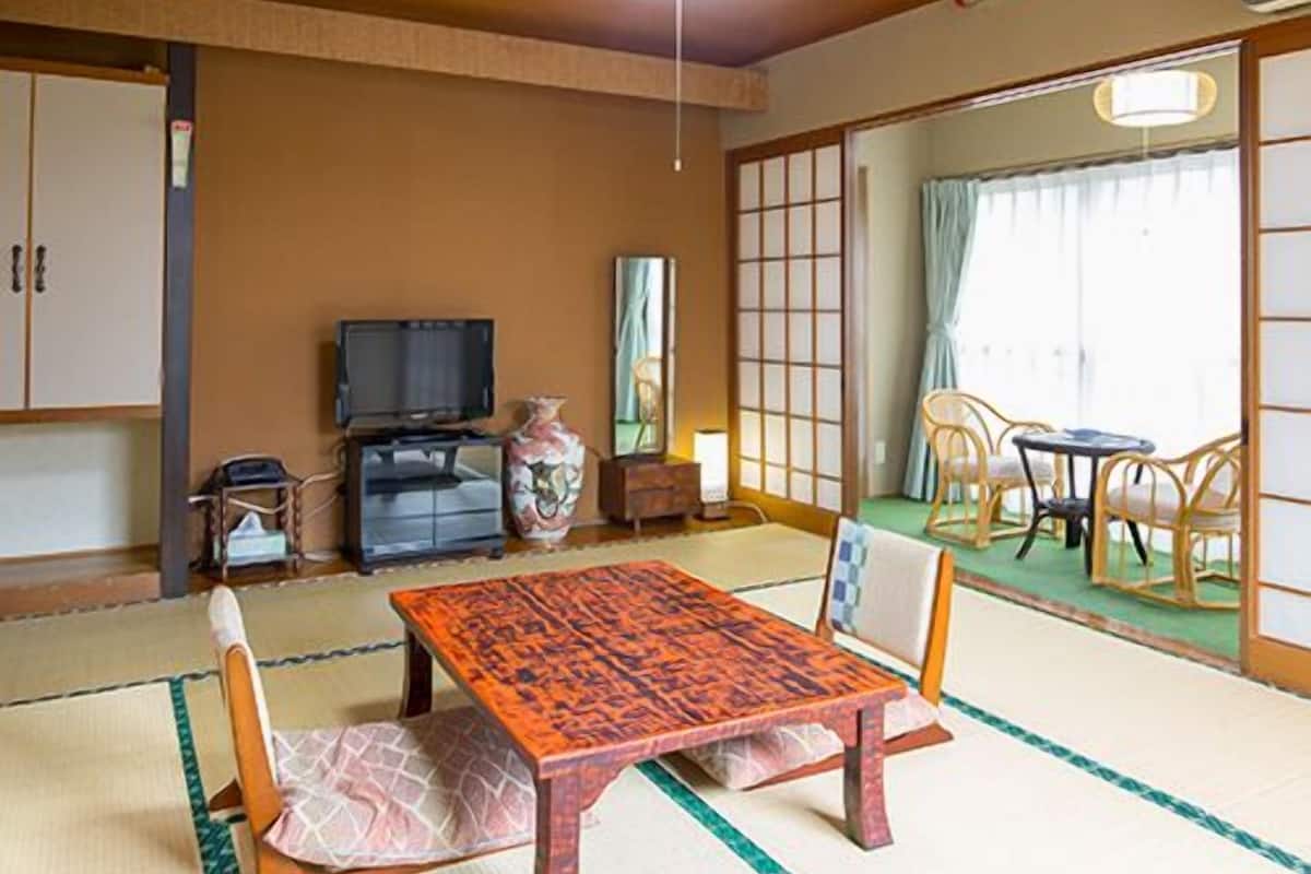 A traditional Japanese room with tatami flooring, a low wooden table, a television, and sliding doors.