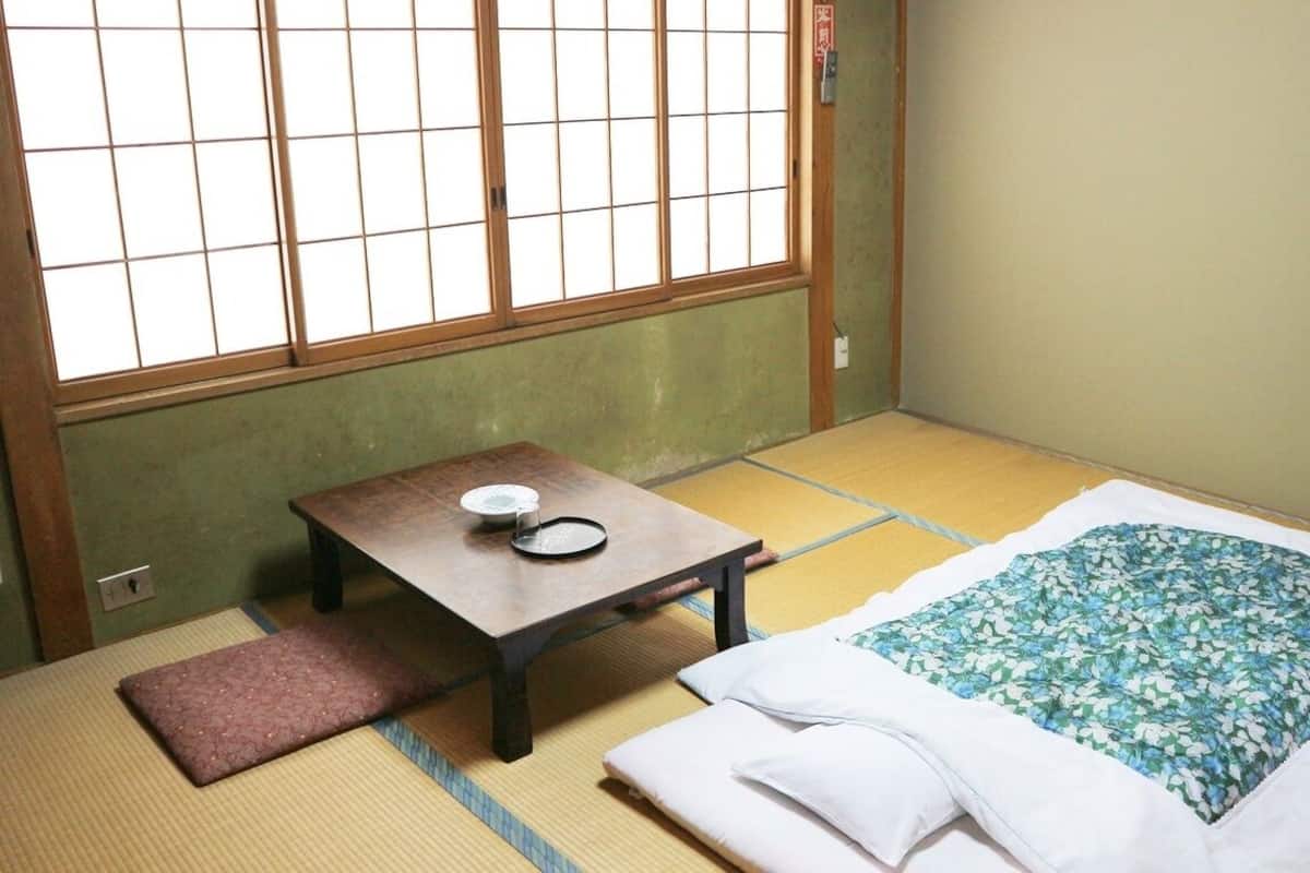 A tatami mat room with a futon bed, a small table with a plate and a cup, and a shoji screen.