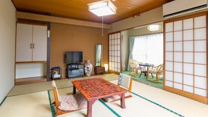 A traditional Japanese room with tatami flooring, a low table with cushions, a television, and sliding doors. - Okuyama (Shinjo)