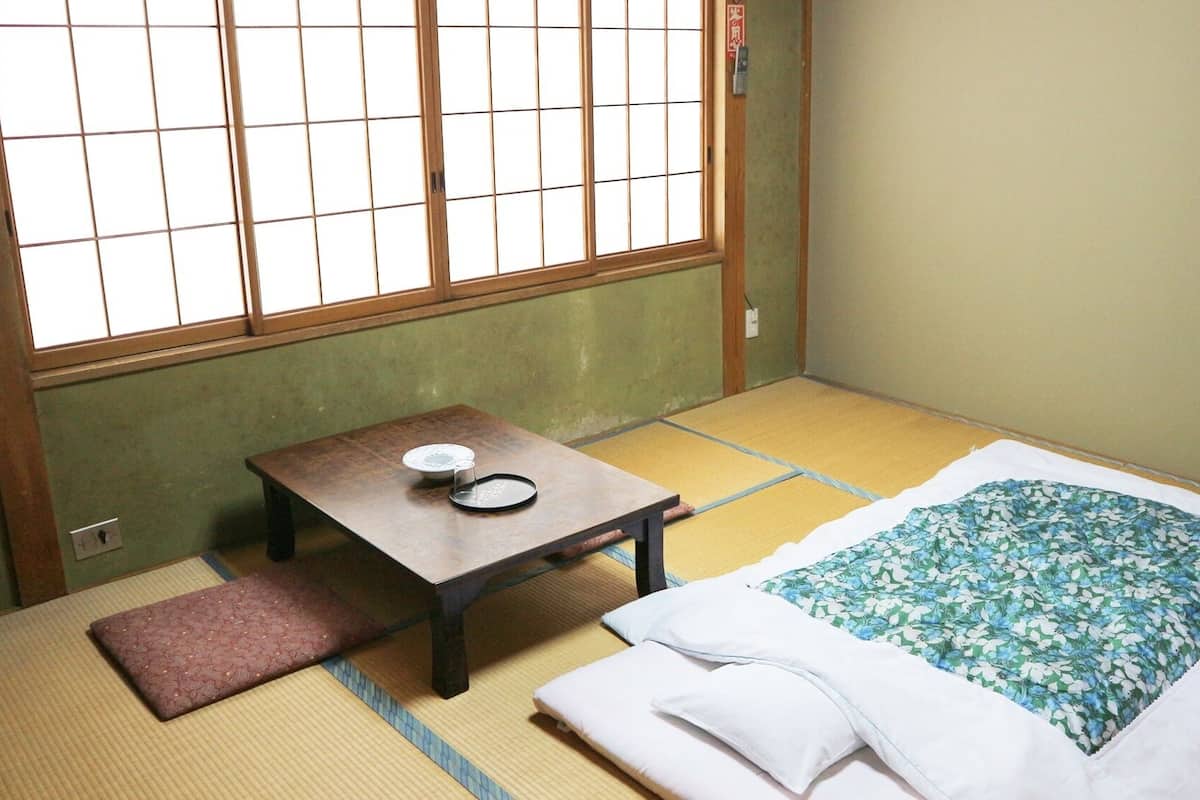 A traditional Japanese room with tatami flooring, a low table with a tea set, and a bed with a floral bedspread.