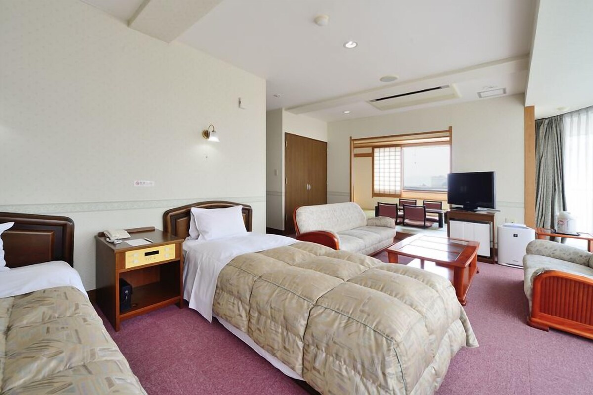 A hotel room with two beds, a sofa, a TV, and a dining area.