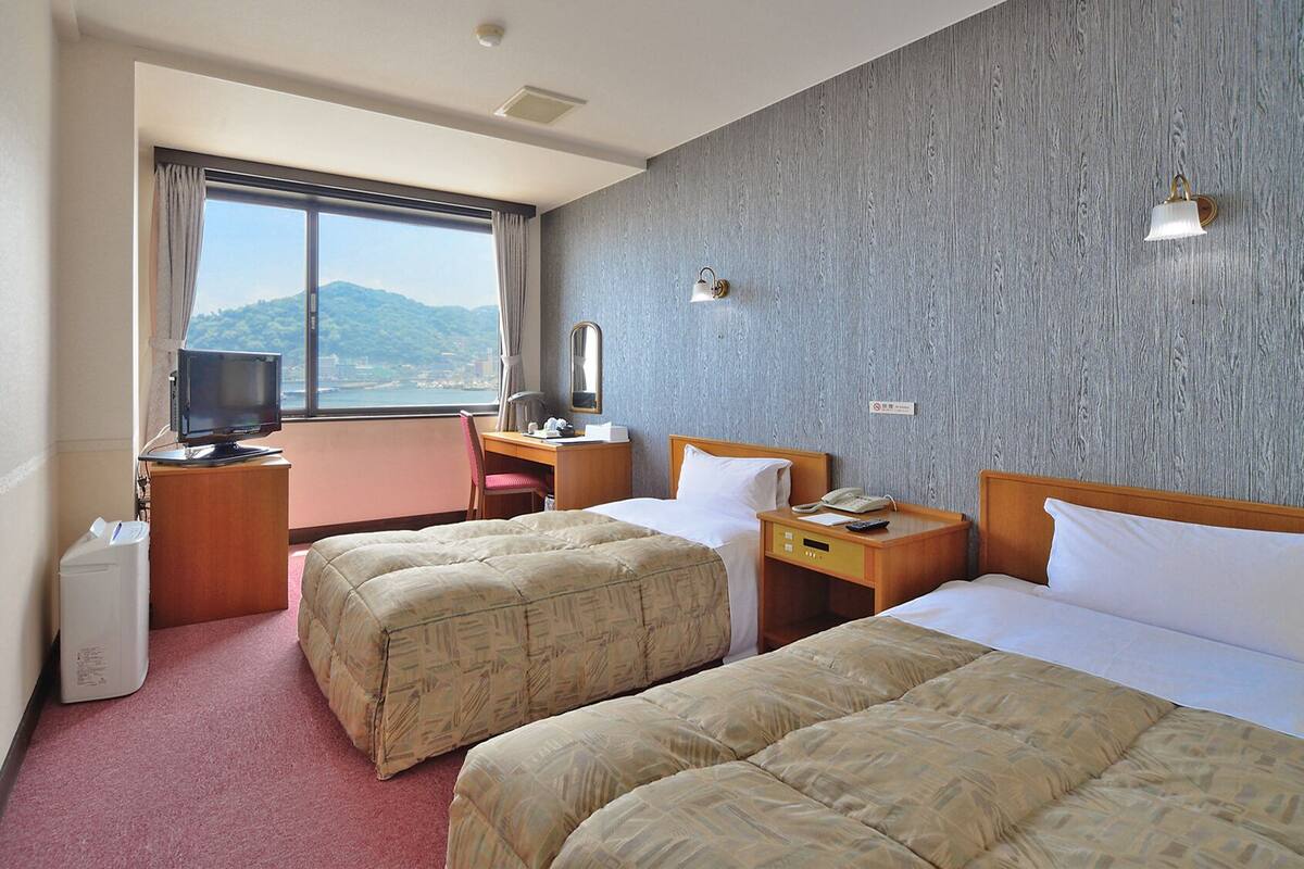 Een hotelkamer met twee bedden, een bureau, een televisie en uitzicht op zee.