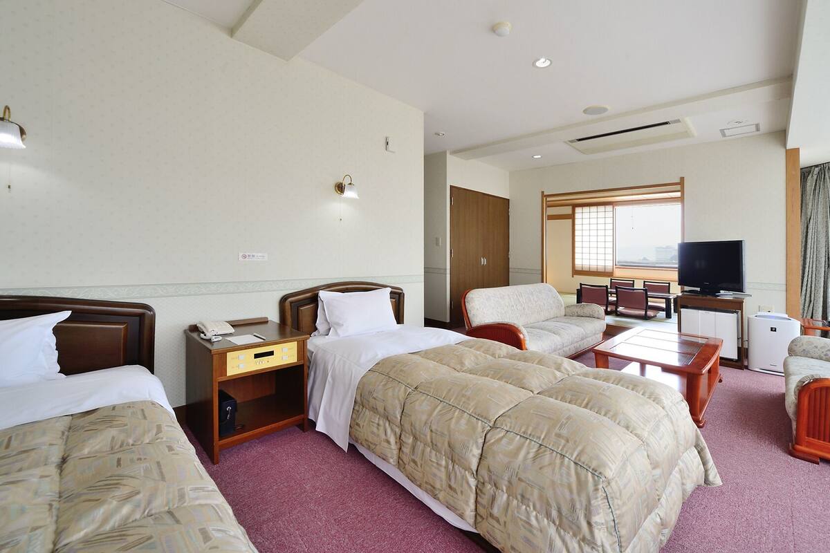 Een hotelkamer met twee bedden, een bureau, een stoel, een televisie en uitzicht op de stad.
