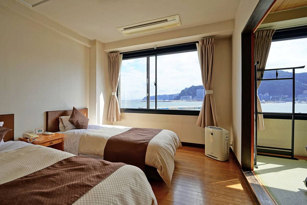 Een hotelkamer met twee bedden, een raam met uitzicht op zee en een airconditioning.