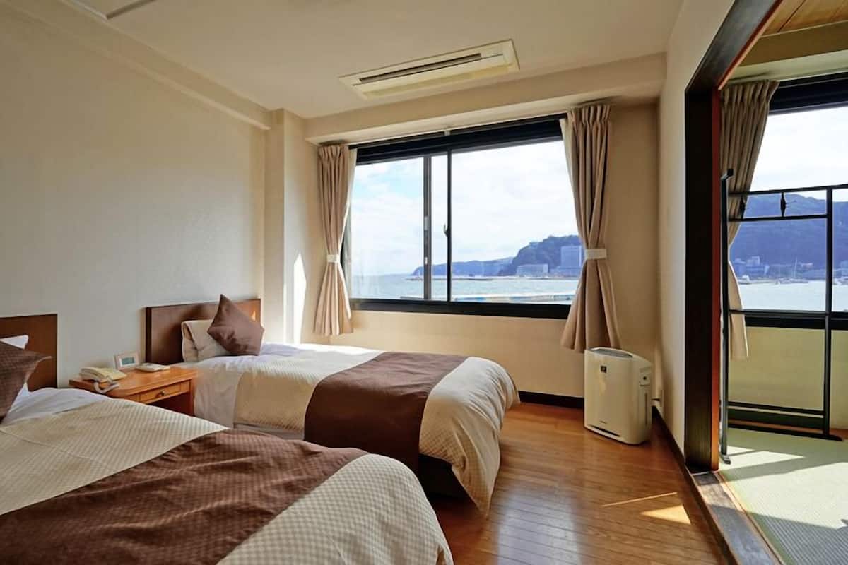 Een hotelkamer met twee bedden, een groot raam met uitzicht op de zee en een balkon.