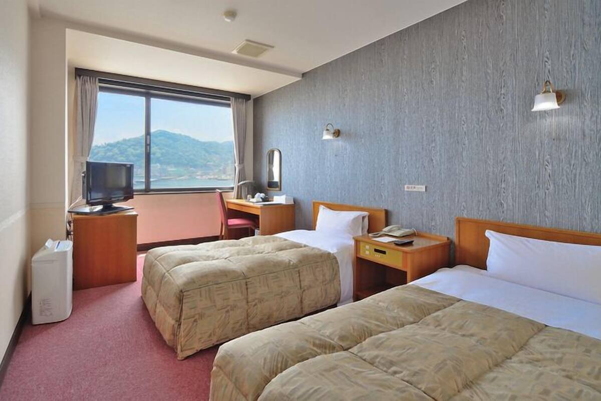 Hotelkamer met twee bedden, een bureau, een stoel, een televisie en een raam met uitzicht op de bergen.