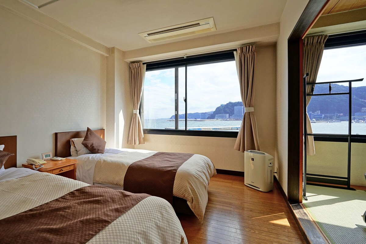 Una camera d'albergo con due letti, una finestra vista mare e un condizionatore.
