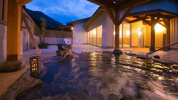 A spa area with a hot spring, wooden deck, and a building with large windows.