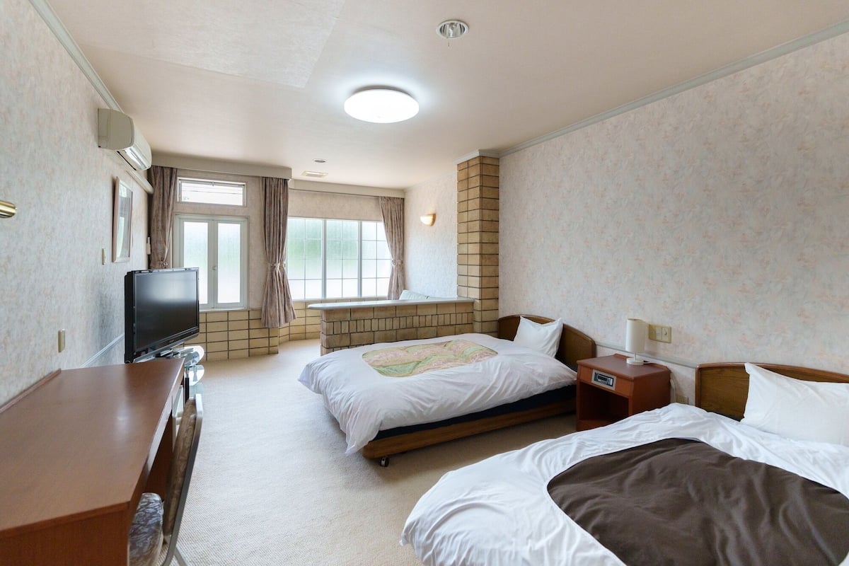 A hotel room with two beds, a TV, a desk, and a window with curtains.