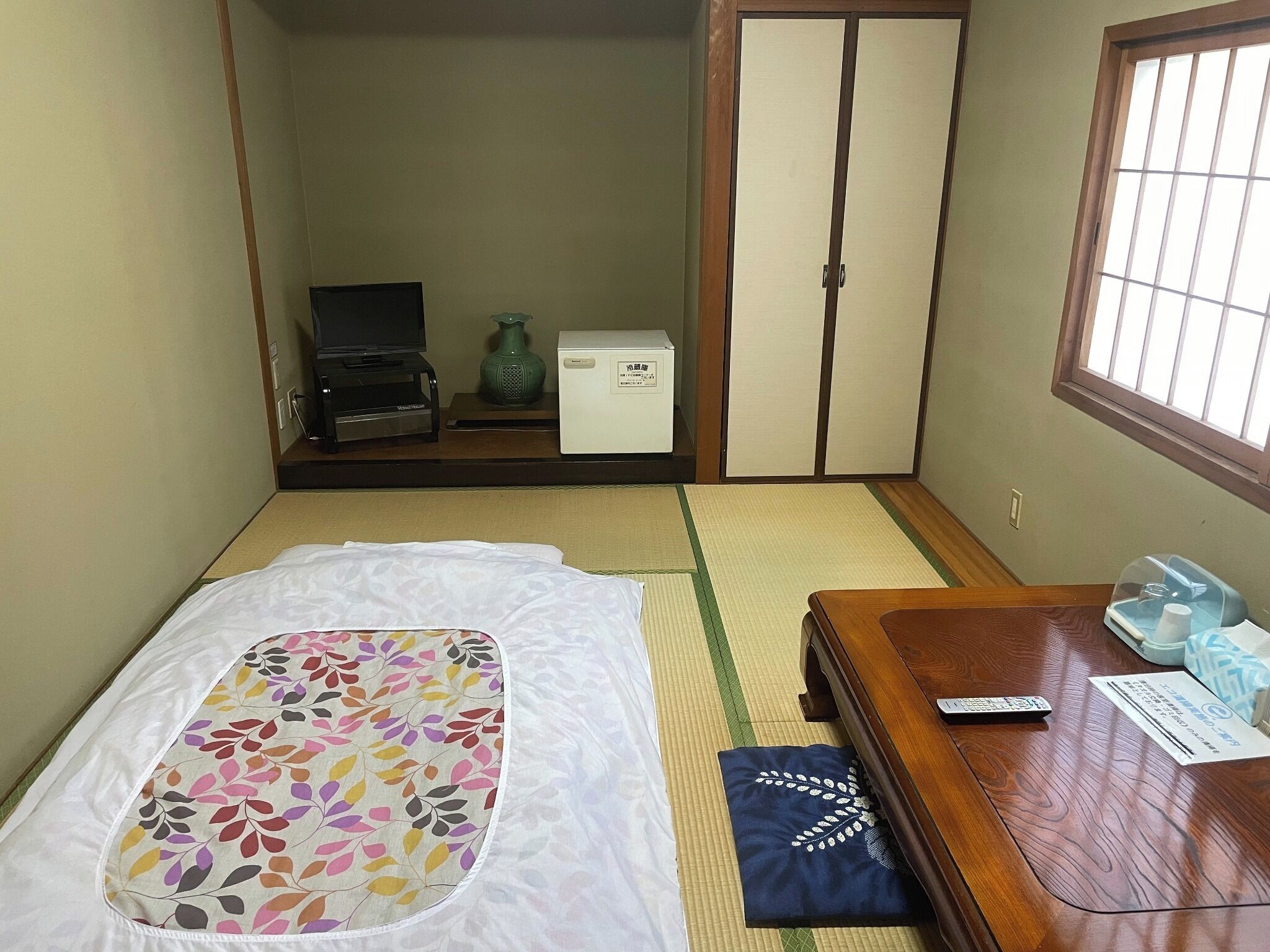 Une chambre avec un lit, une table en bois, une télévision et une armoire.