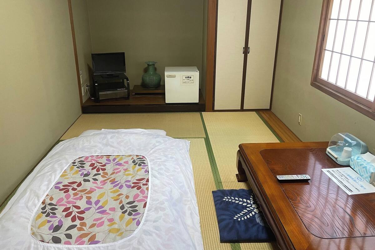 A room with a bed, a wooden table, a TV, and a wardrobe.