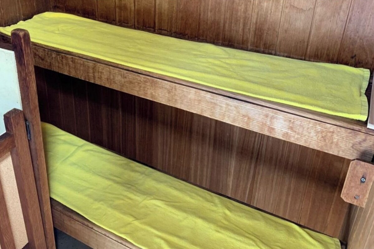 A bunk bed with a yellow mattress and wooden frame.