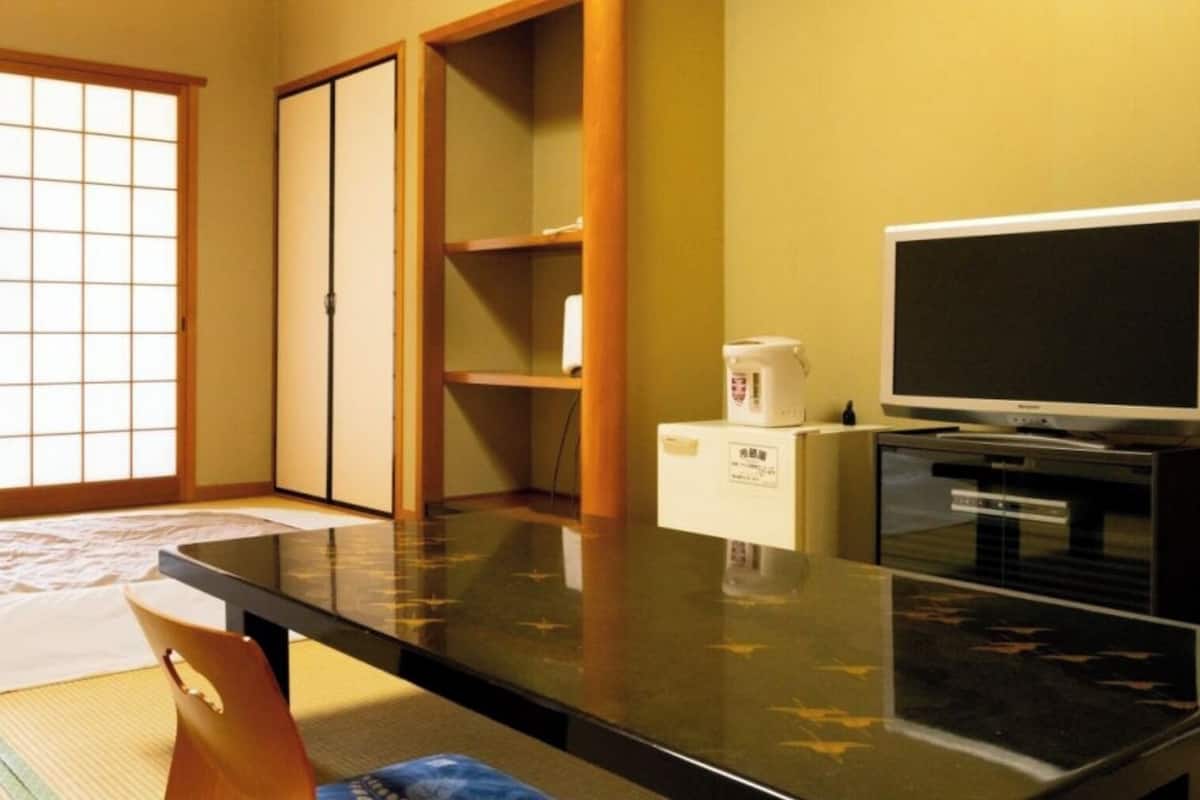 A room with tatami flooring, a futon bed, sliding doors, a television, and a microwave.