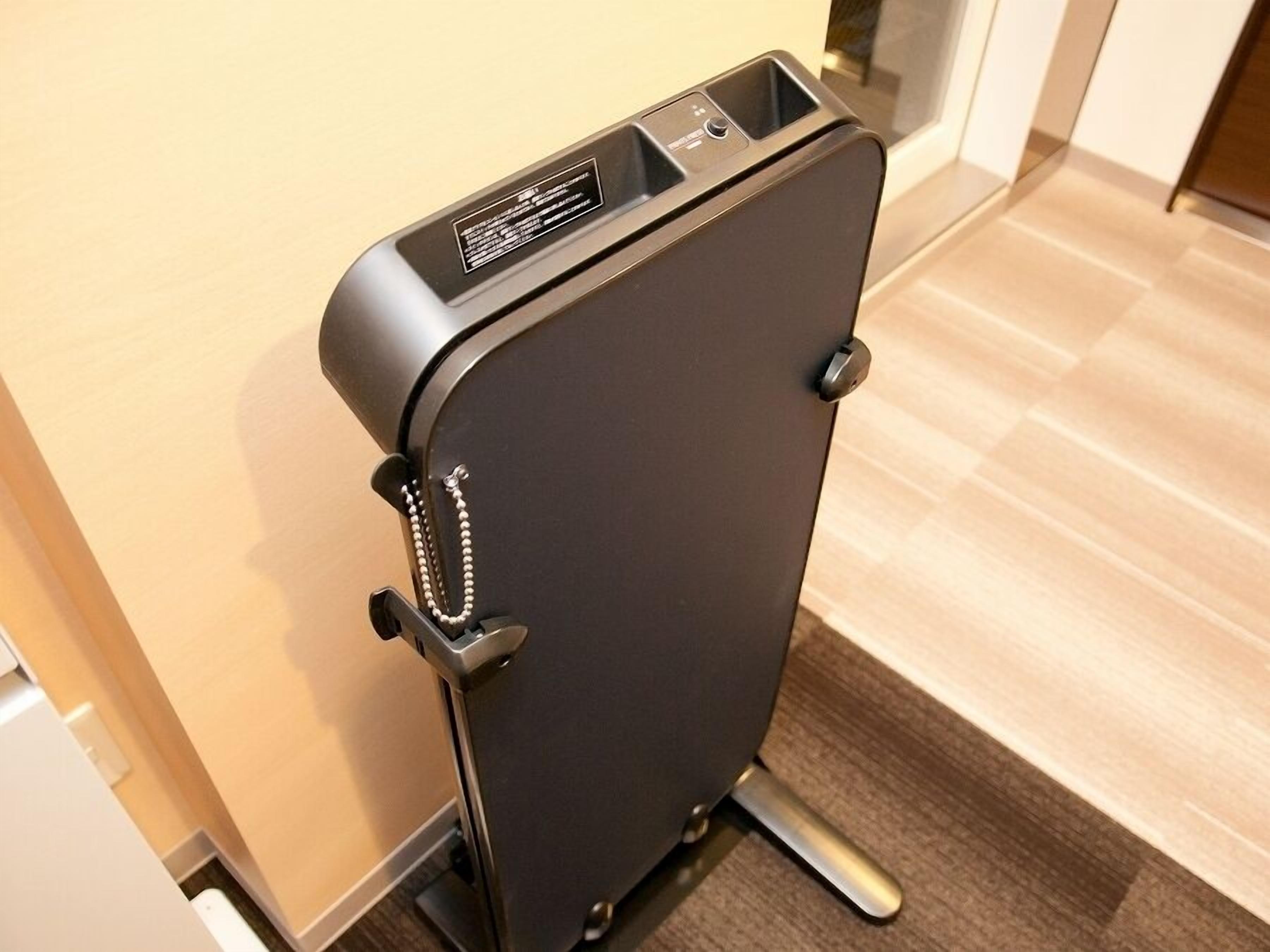 A black suitcase with wheels, a handle, and a chain strap, placed on a wooden floor.