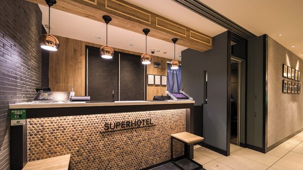 A hotel reception area with a wooden reception desk, three pendant lights, and a wall with a honeycomb pattern. - Super Hotel Kofu Showa Inter (Showa)