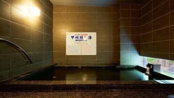 A hot spring area with tiled walls, a signboard, and a metal railing.