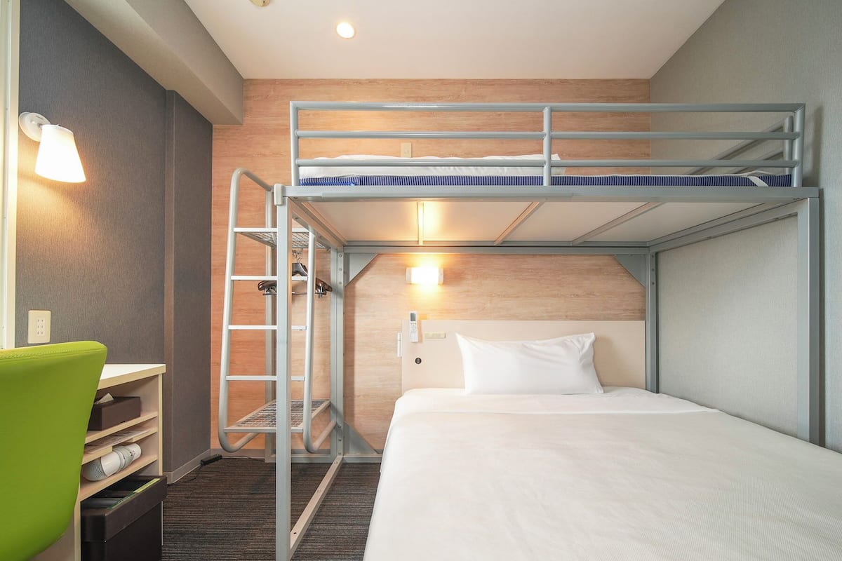 Een slaapkamer met stapelbed, bureau en stoel, een trapje en een wandlamp.