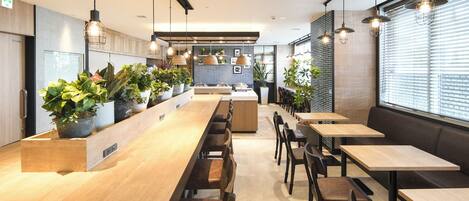 A modern cafe with a long wooden counter, multiple seating areas, and potted plants.