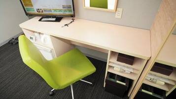 A hotel room with a desk, a bright green chair, a computer monitor displaying the SuperHotel website, a mirror, and a small shelf with a book and a remote control.