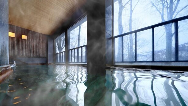 Una piscina interior espaciosa con reflejos nítidos en el suelo, ventanas amplias y un moderno techo de madera.
