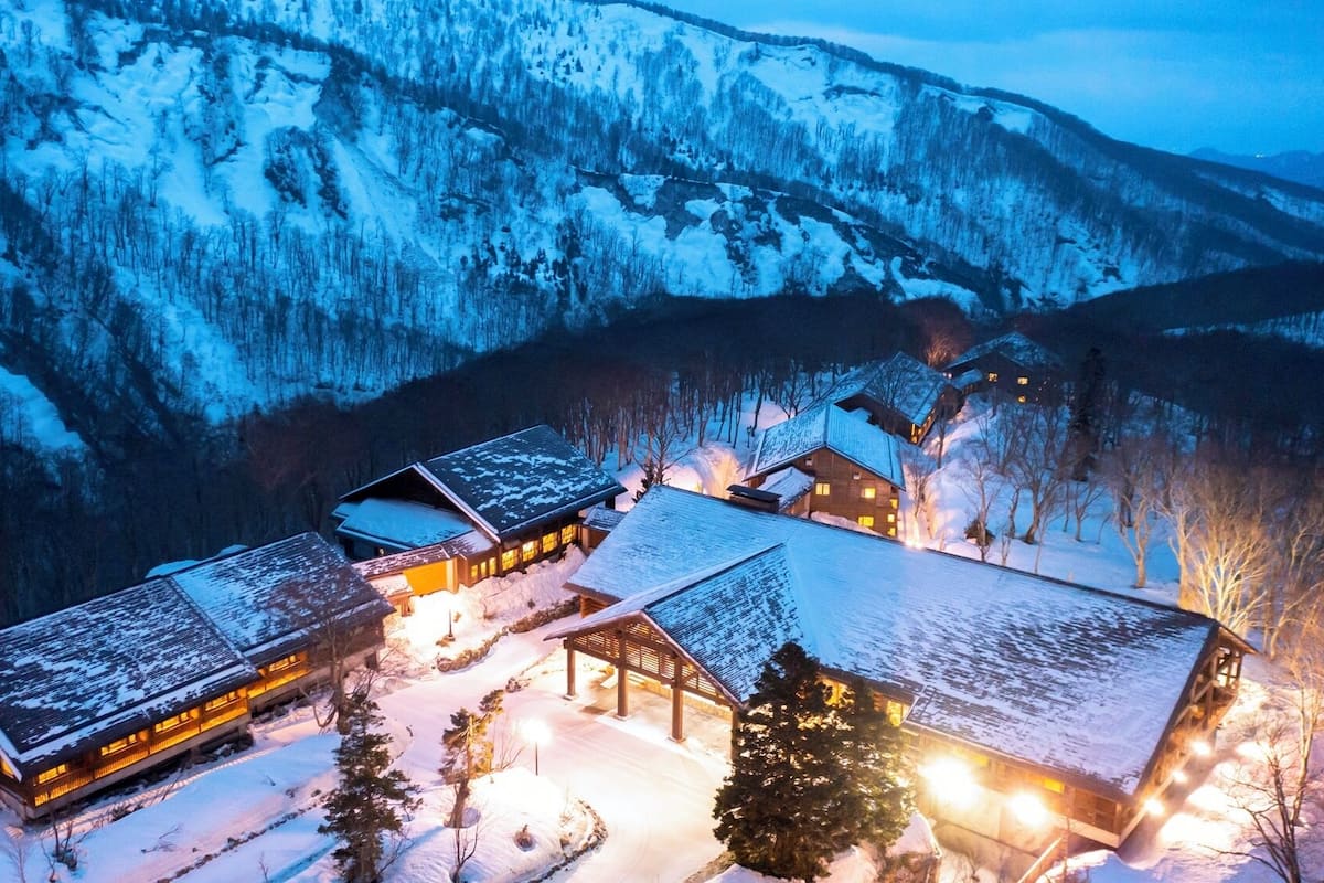 Eine schneebedeckte Lodge mit mehreren Gebäuden, einer Holzdiele und einer verschneiten Landschaft.